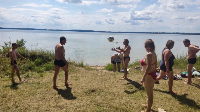 Colvēki ezera pludmalē spēlē bumbu