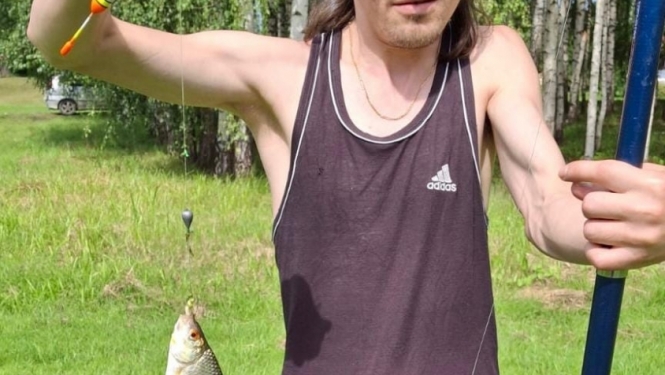 Vīrietis ar makšķeri un zivi rokās
