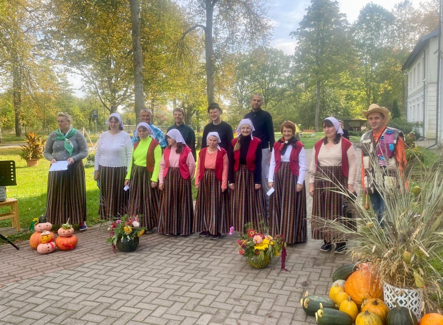 Cilvēku grupa tautastērpos, uz bruģa- dārzeņi