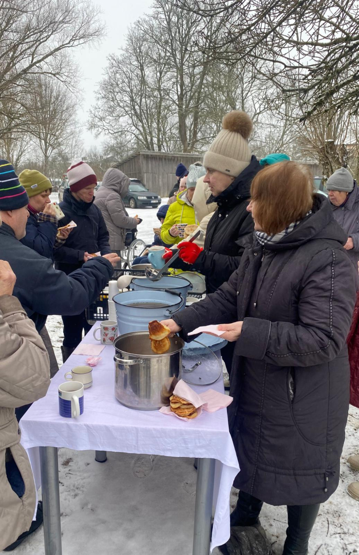 Cilvēki ārā pie galda, uz galda trauki ar dzērieniem