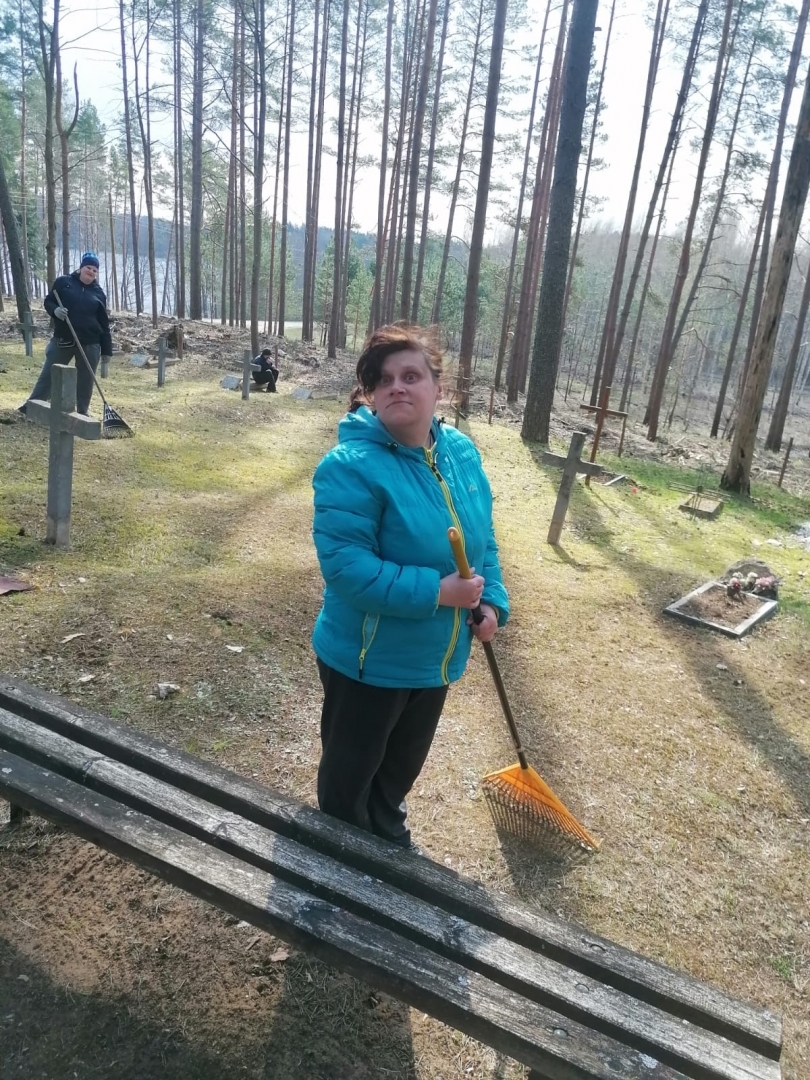 Sieviete zilā jakā grābj koku lapas